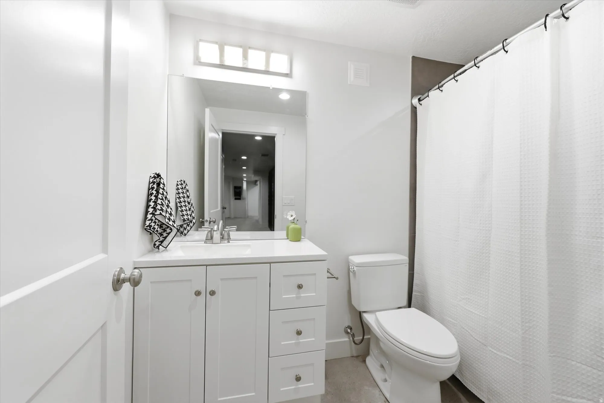 Bathroom featuring a white vanity with panel cabinetry and a light-toned countertop, a rectangular mirror, a chrome-finish faucet, and a toilet