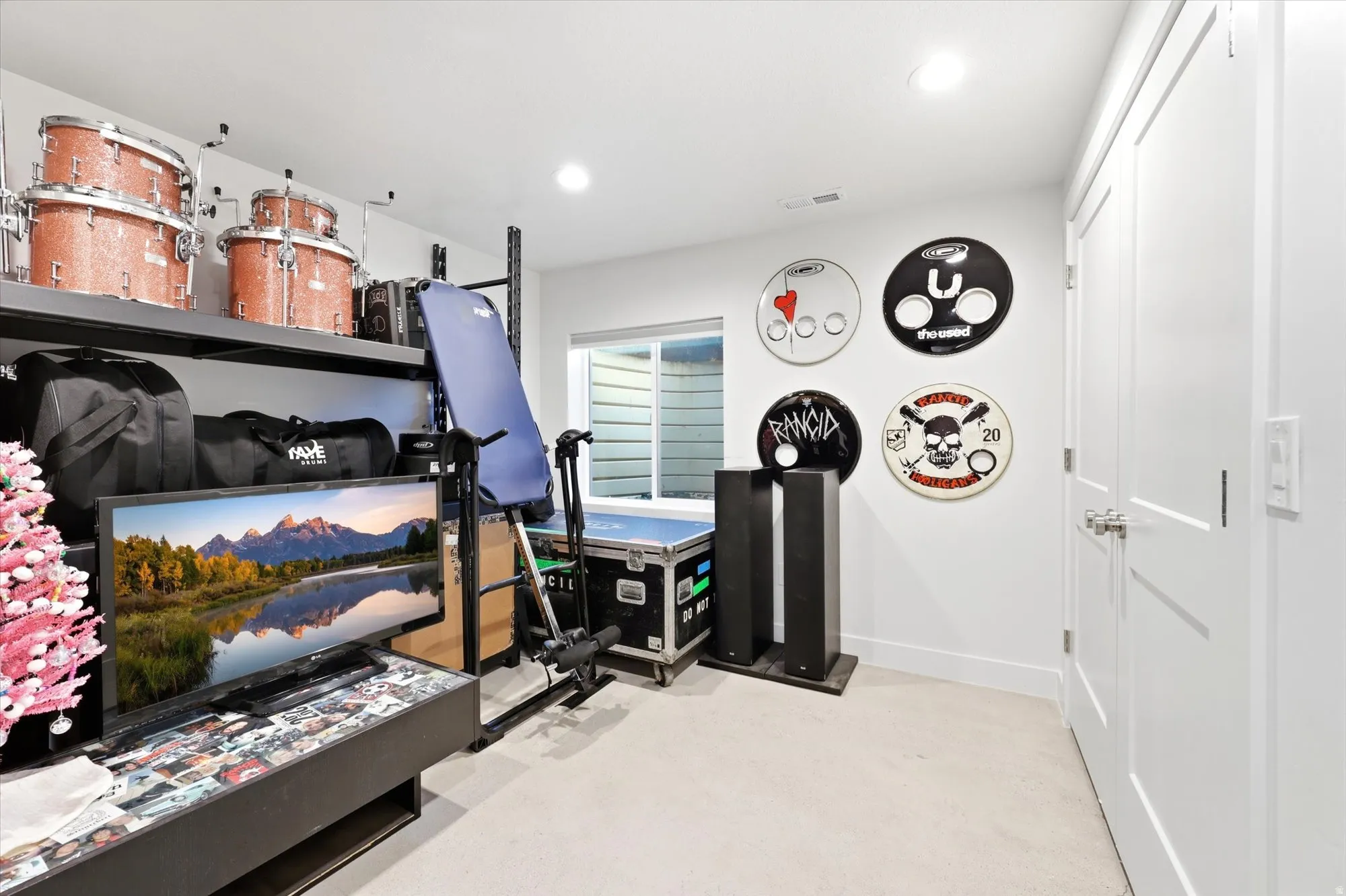 Recessed lighting illuminates this versatile space, featuring white walls, light carpet flooring, and a window with horizontal blinds