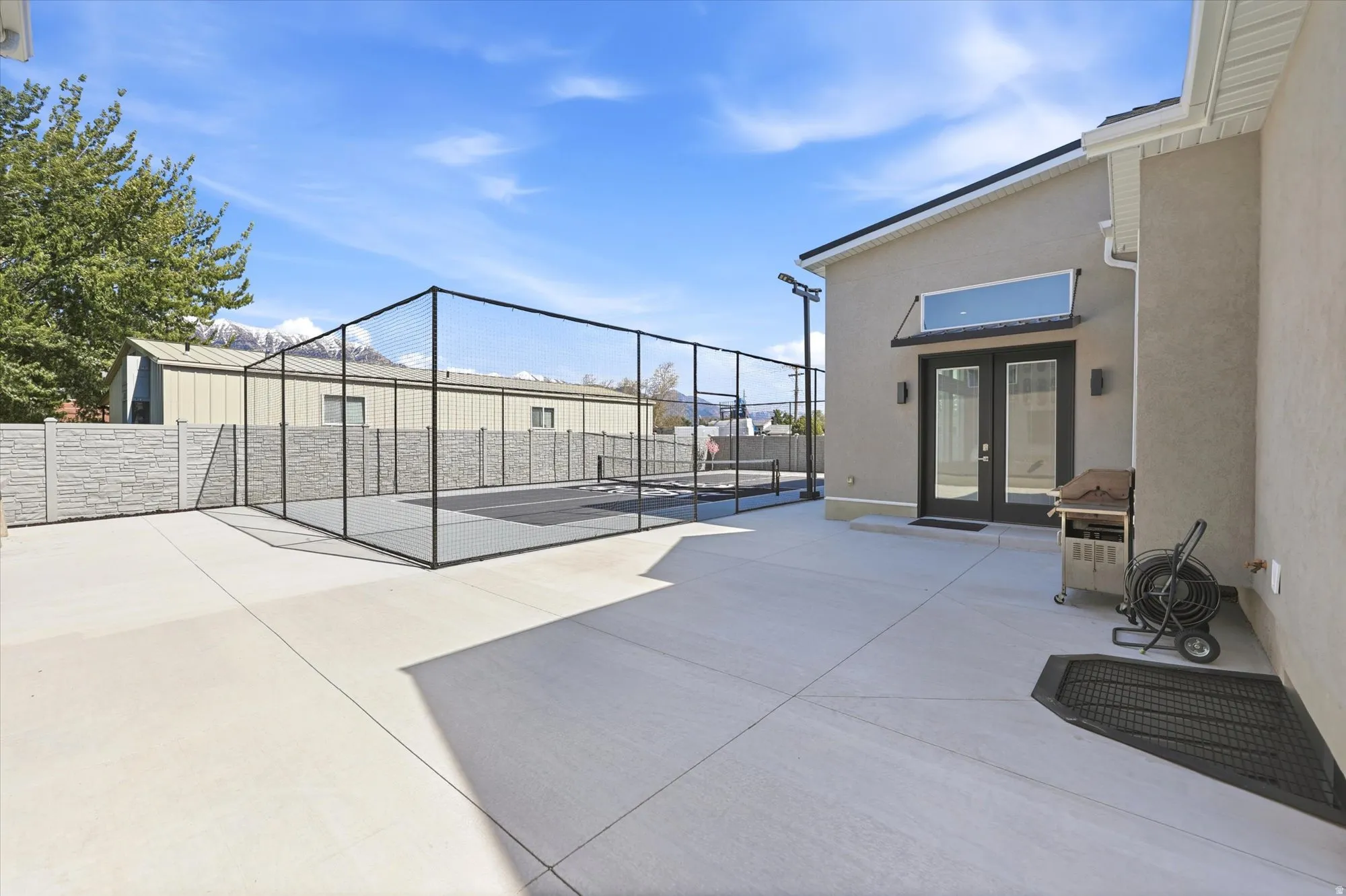 Spacious concrete patio featuring a fenced sport court, contemporary exterior lighting, and double glass French doors