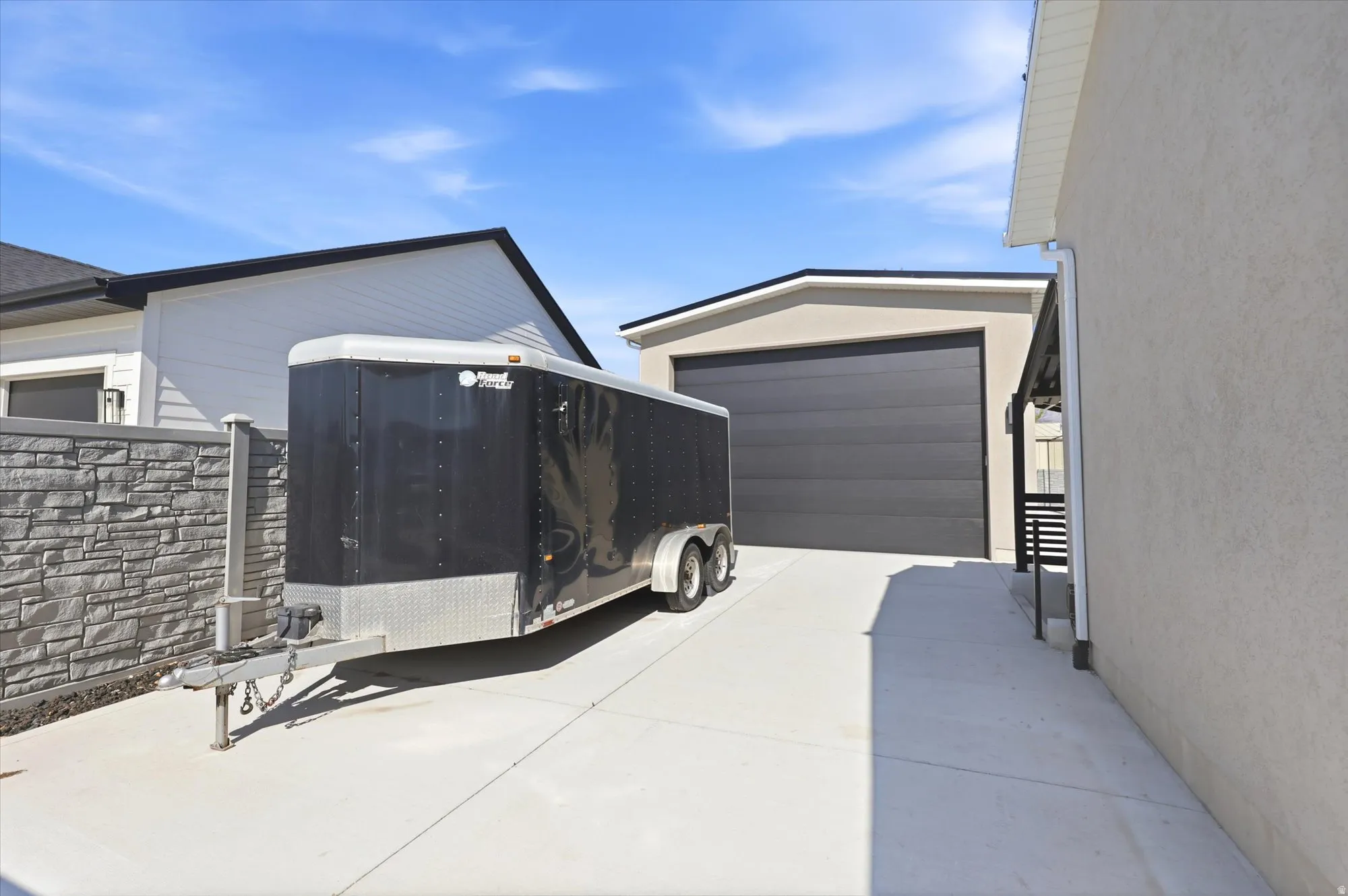 Concrete driveway providing access to a detached garage with a dark gray door and an adjacent stone-finish privacy wall