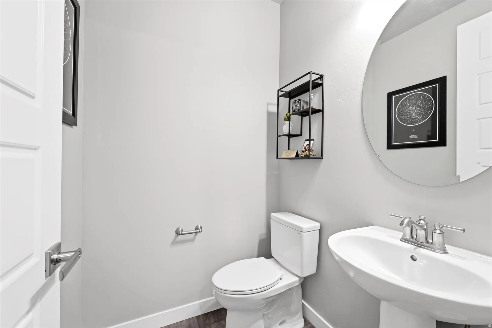 Pedestal sink with a chrome faucet, round wall mirror, and a white toilet