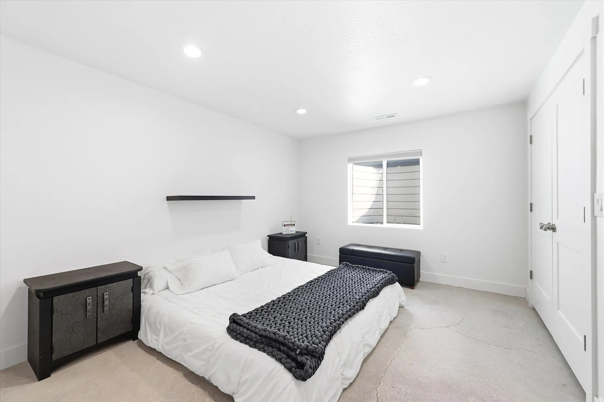Recessed lighting illuminates this bright room featuring a single window, white trim, and a built-in wall shelf
