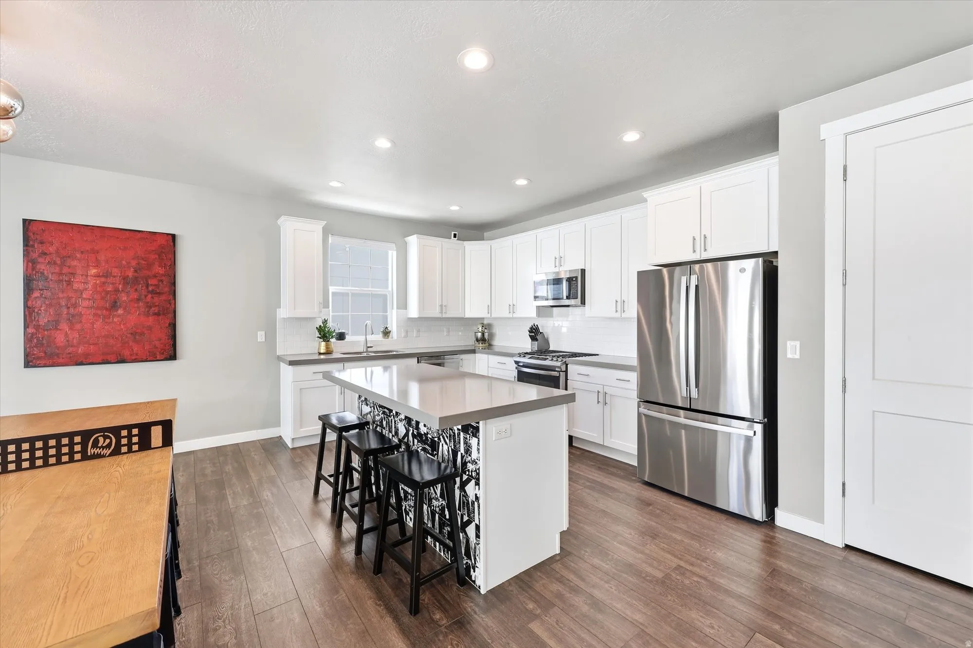 Modern kitchen featuring wood-finish flooring, a central island with bar seating, white shaker cabinetry, stainless steel appliances, and light-toned countertops