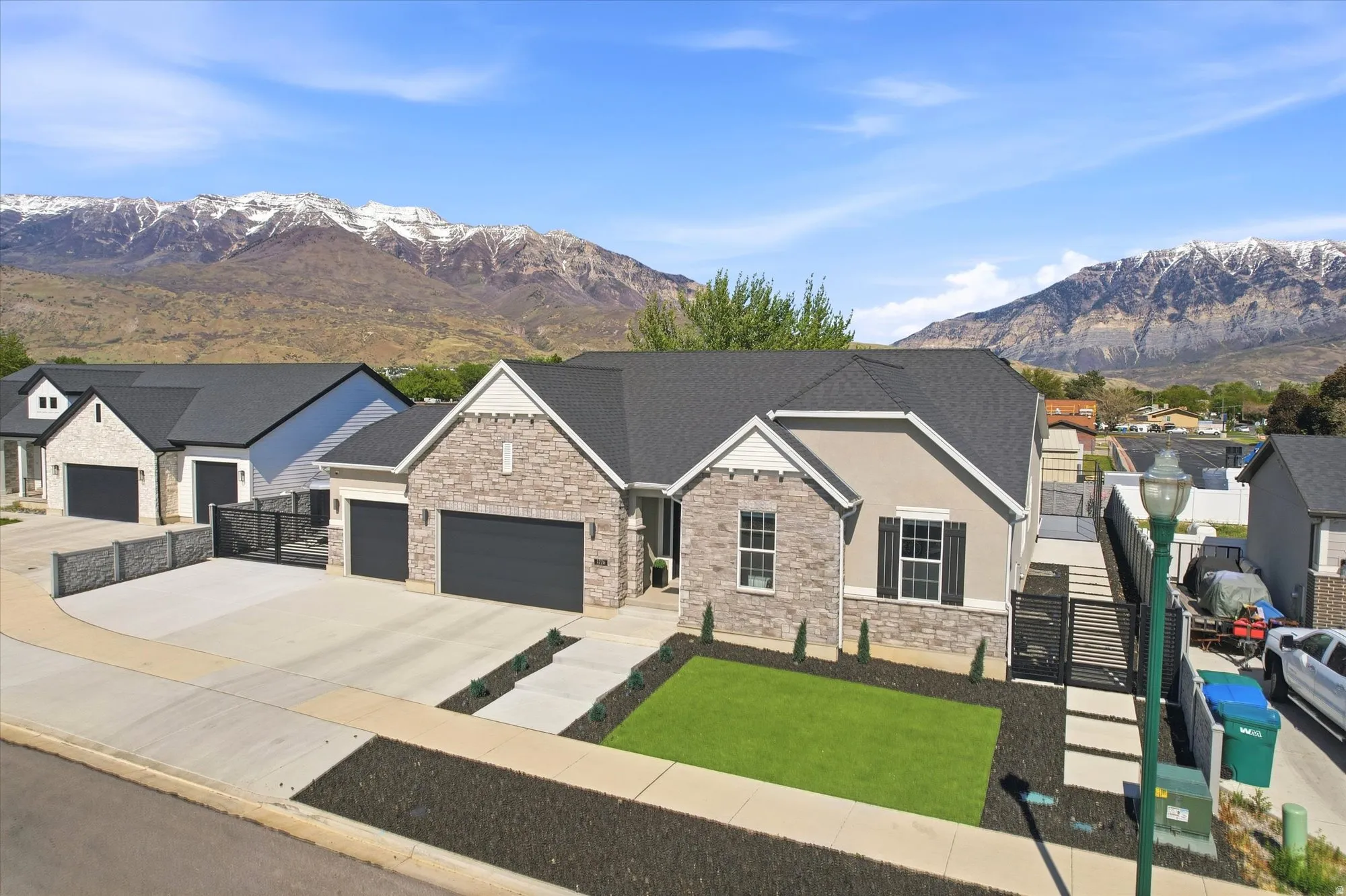 Modern ranch-style residence featuring a stone and stucco exterior, dark asphalt shingle roof, and a three-car garage