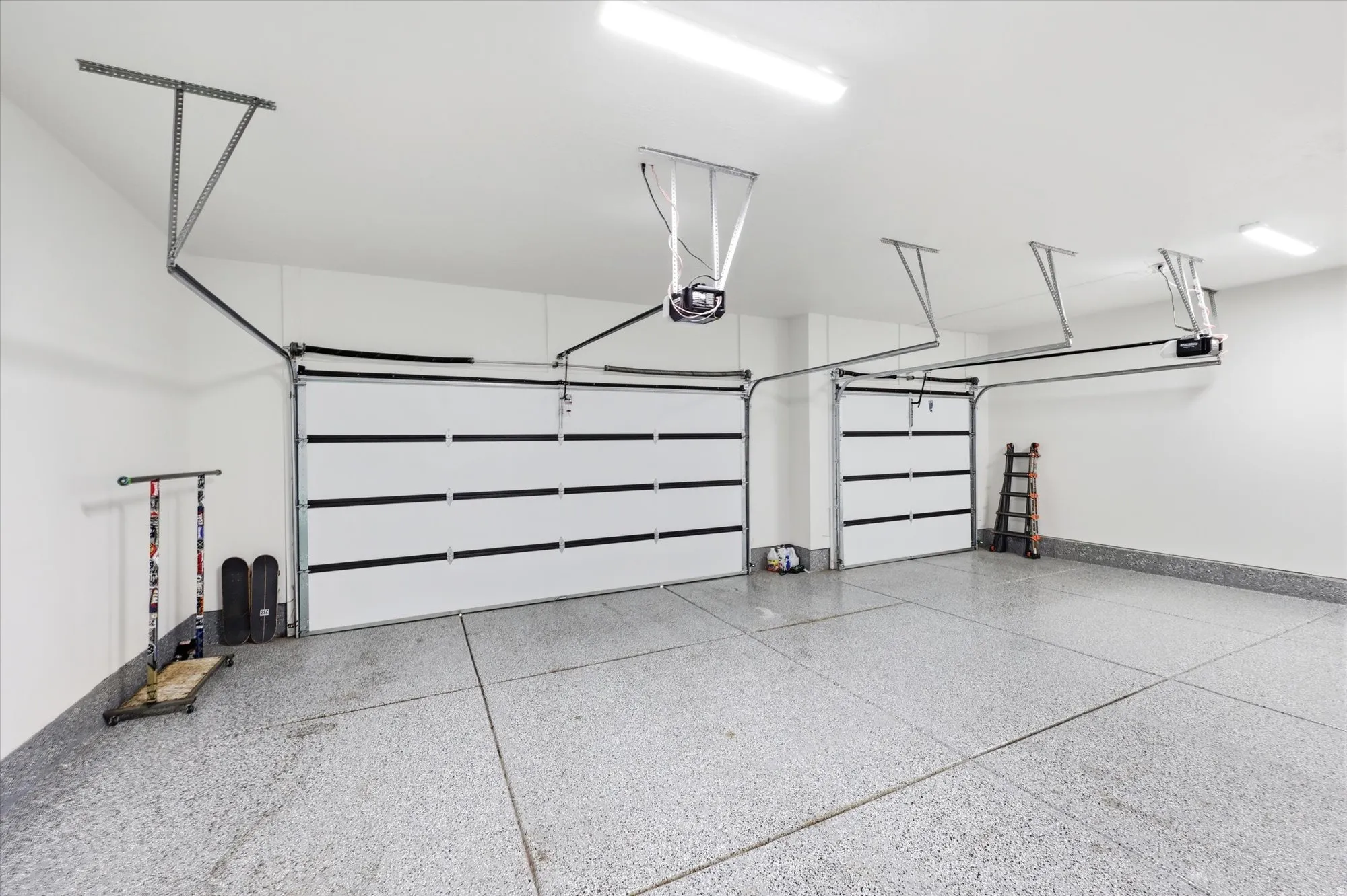 Spacious garage featuring two overhead doors, a speckled epoxy floor, white walls, and overhead fluorescent lighting