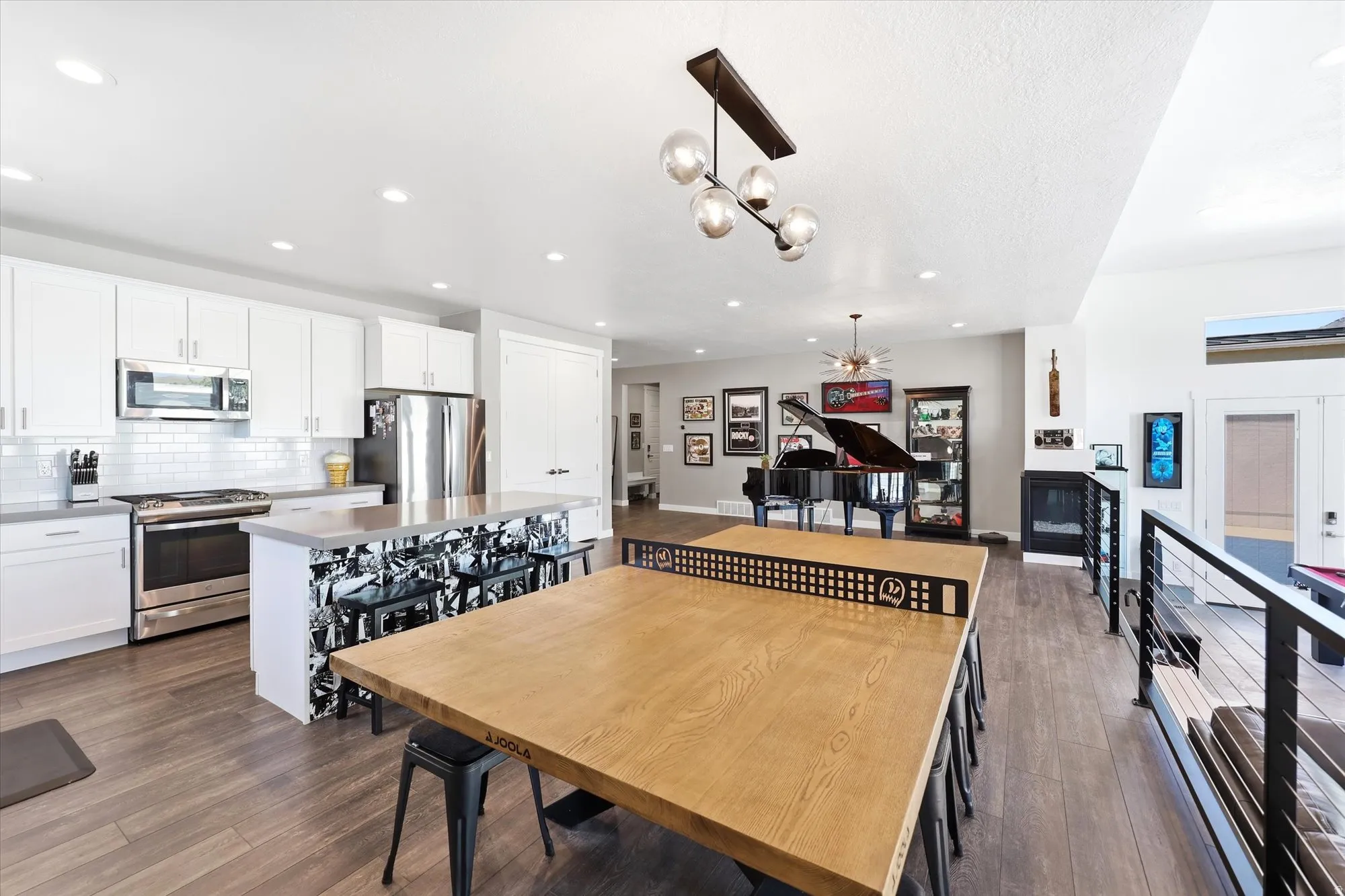 Open-concept common area featuring wood-finish flooring, a contemporary chandelier, recessed lighting, a white subway tile backsplash, and a modern fireplace with a black metal grate