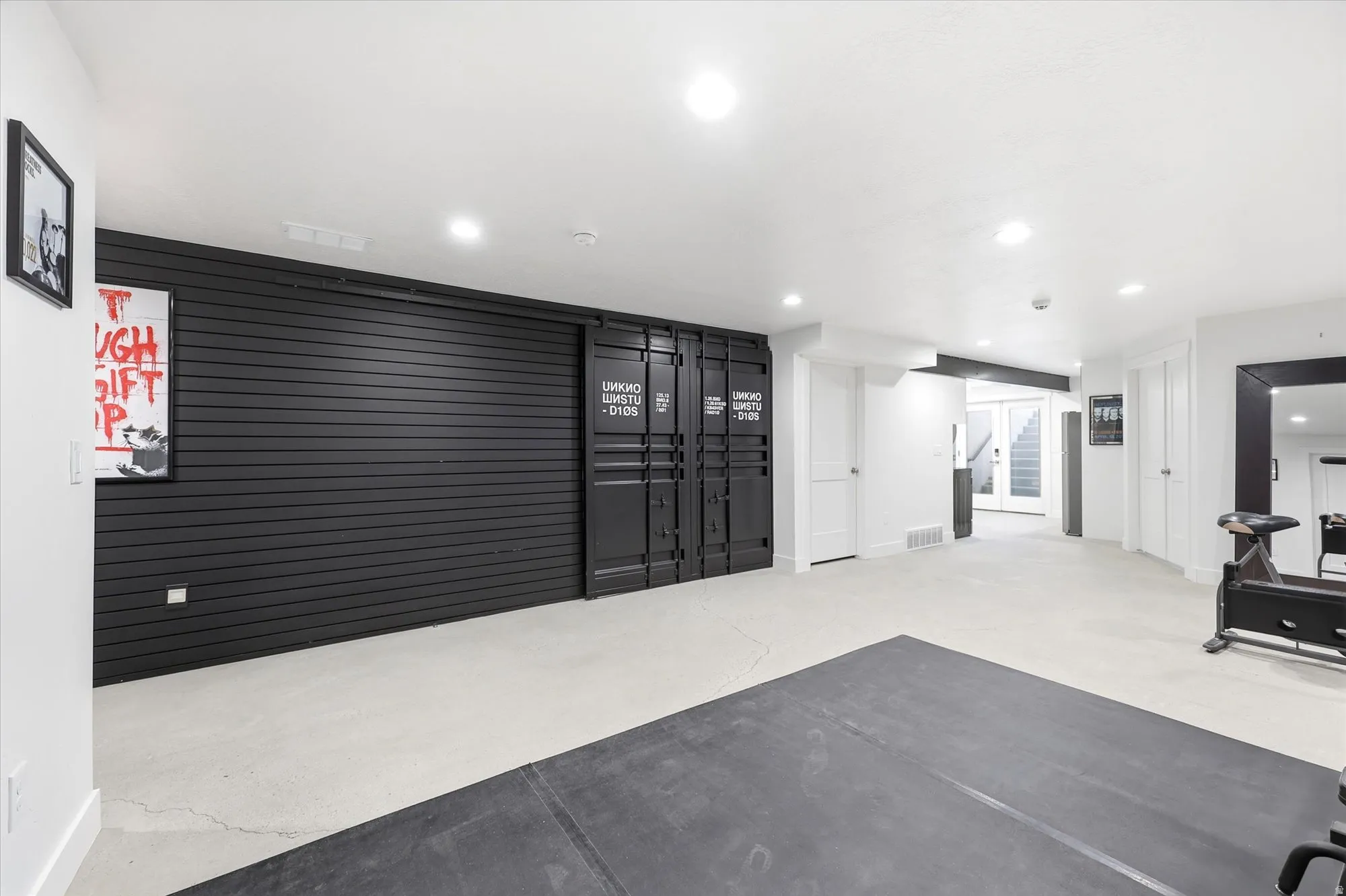 Spacious recreation area featuring a black slatwall accent, built-in storage with industrial-style doors, light-toned concrete flooring, and recessed lighting