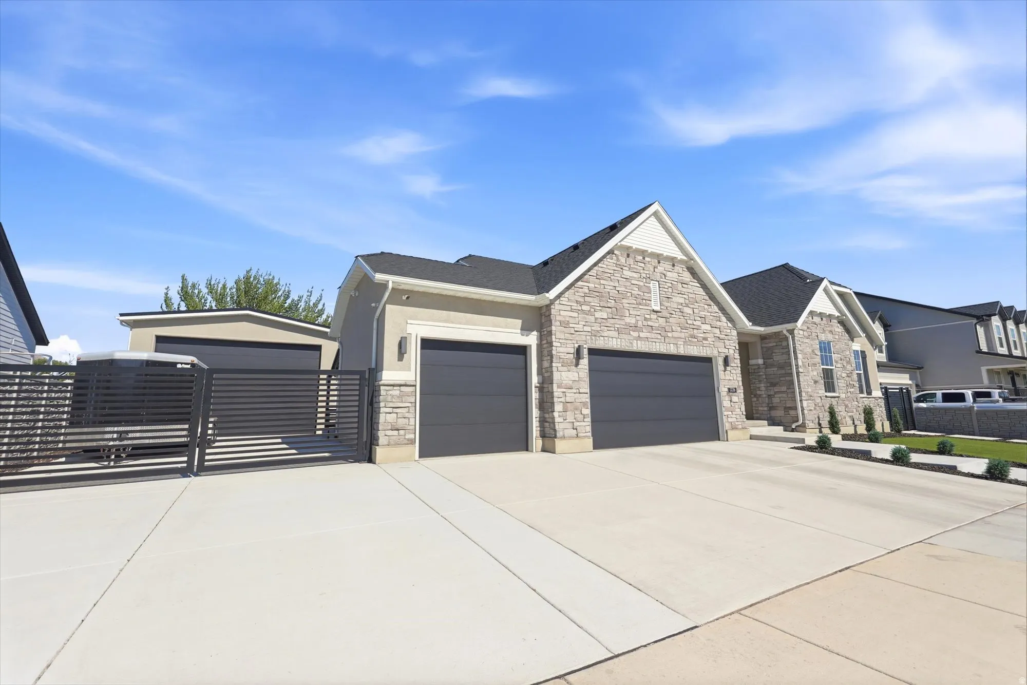 Contemporary residence featuring a stone and stucco facade, a two-car garage with modern doors, an additional detached garage structure, a dedicated concrete drive, and a horizontal slat gate