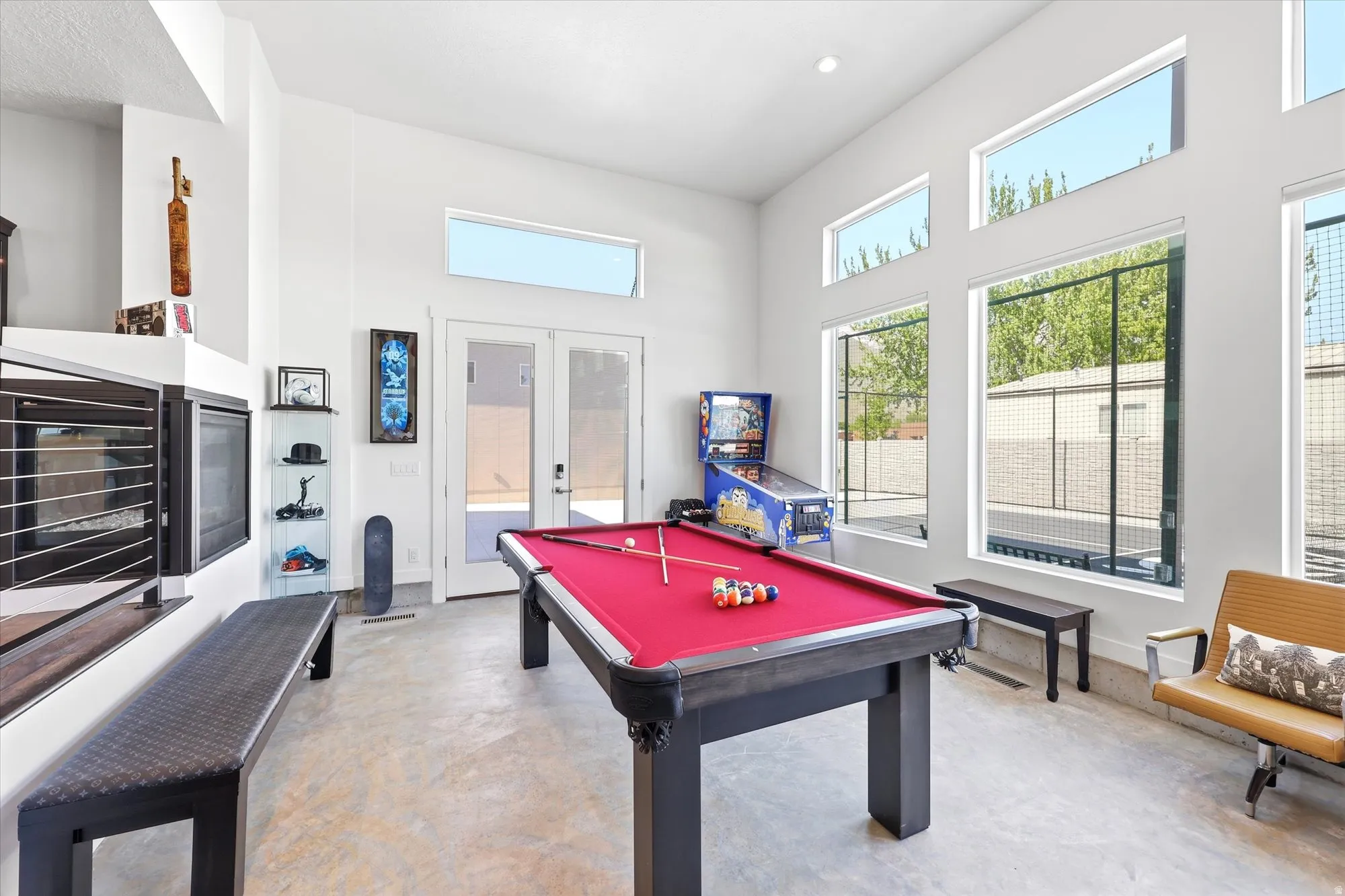 Spacious recreation room featuring high ceilings, multiple large windows, light-toned flooring, a built-in fireplace, and French patio doors