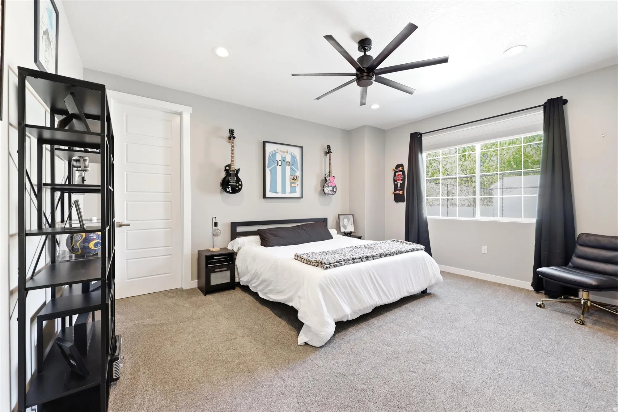 Carpeted room featuring a large window with black drapery, a multi-blade ceiling fan, a contemporary solid-panel interior door, and recessed lighting