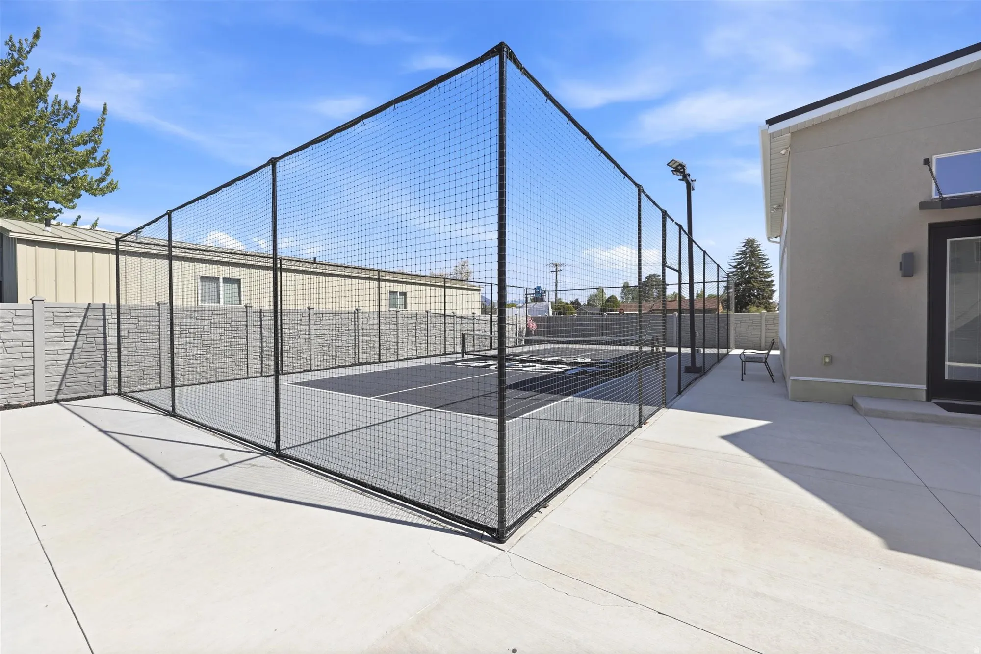 Outdoor sports court featuring a black net enclosure, integrated lighting, and a concrete perimeter