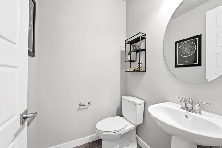 Pedestal sink with a chrome faucet, round wall mirror, and a white toilet