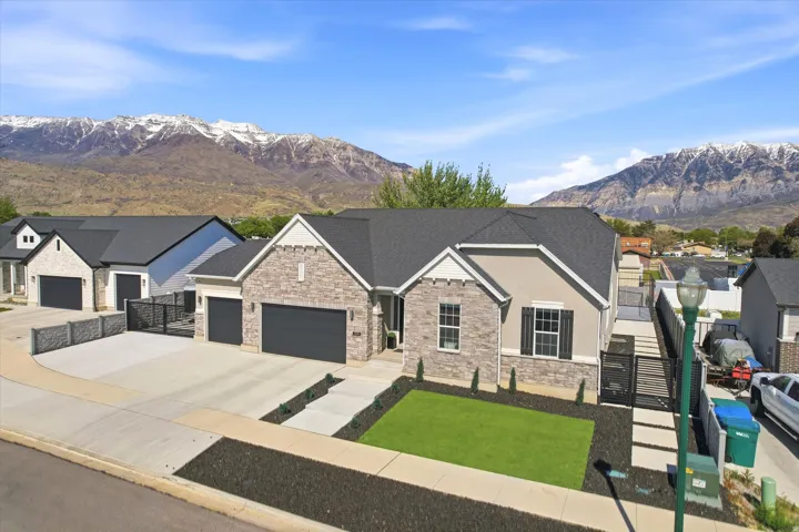 Modern ranch-style residence featuring a stone and stucco exterior, dark asphalt shingle roof, and a three-car garage