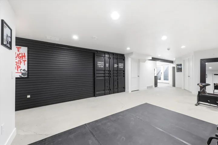 Spacious recreation area featuring a black slatwall accent, built-in storage with industrial-style doors, light-toned concrete flooring, and recessed lighting