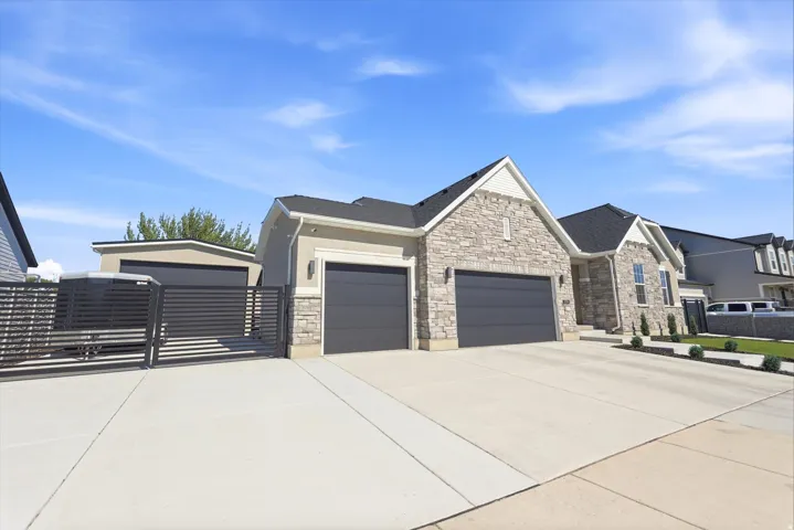 Contemporary residence featuring a stone and stucco facade, a two-car garage with modern doors, an additional detached garage structure, a dedicated concrete drive, and a horizontal slat gate