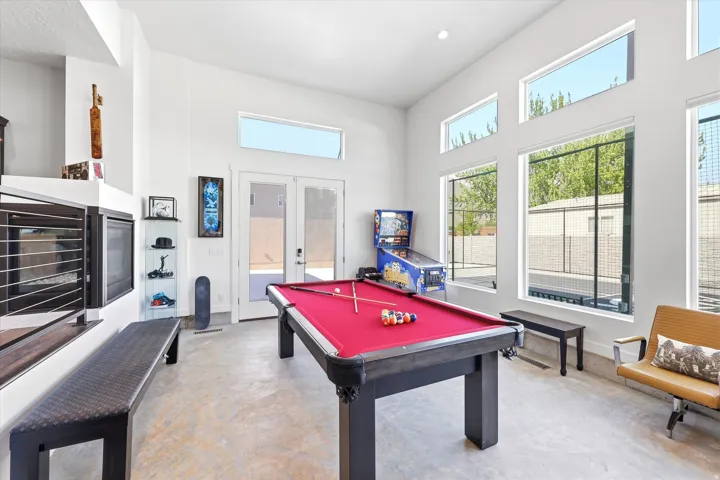 Spacious recreation room featuring high ceilings, multiple large windows, light-toned flooring, a built-in fireplace, and French patio doors