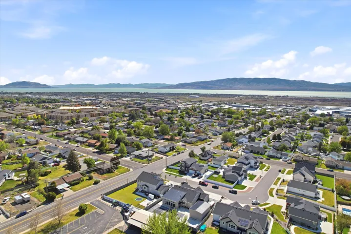 Expansive aerial perspective showcasing a residential neighborhood with a distant body of water and mountain range under a clear sky