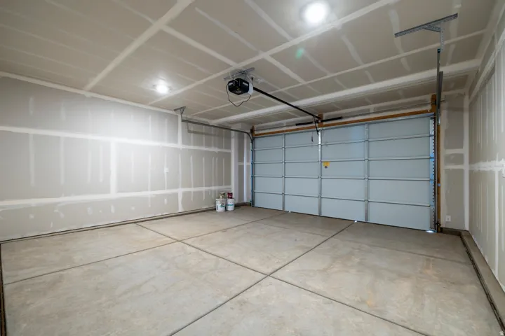 Spacious garage featuring a large overhead door, automatic opener, concrete flooring, and ceiling-mounted lighting