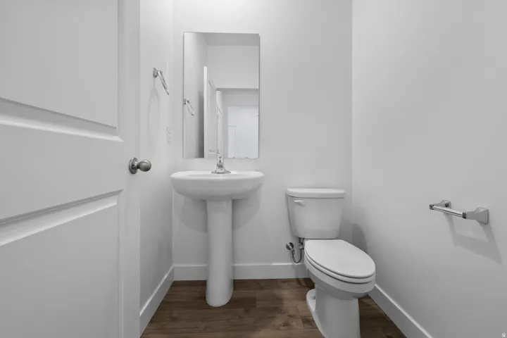 White pedestal sink with chrome faucet, a rectangular mirror, and wood-finish flooring