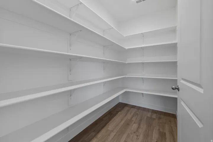 Spacious walk-in pantry featuring extensive white shelving, wood-finish flooring, and a white interior door with a brushed nickel knob