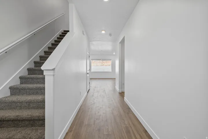 Entryway featuring a carpeted staircase with white handrail, wood-finish flooring, and recessed lighting