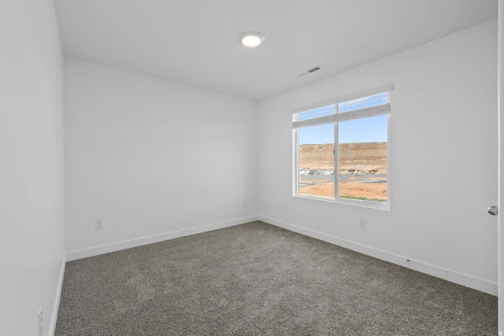 Spacious room featuring a large window, soft grey carpet, recessed ceiling light, and white walls with matching baseboards