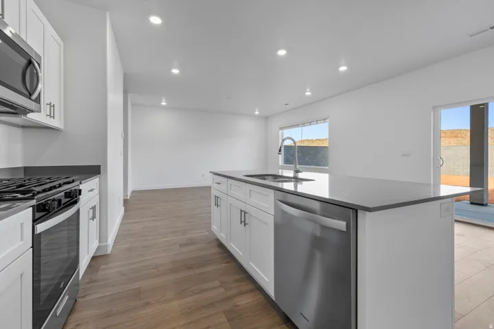 Modern kitchen featuring white cabinetry, stainless steel appliances, a center island with a sink, recessed lighting, and wood-finish flooring