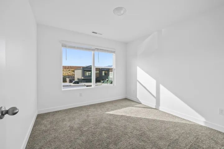 Carpeted room featuring a large window with blinds, white walls, and a ceiling-mounted light fixture