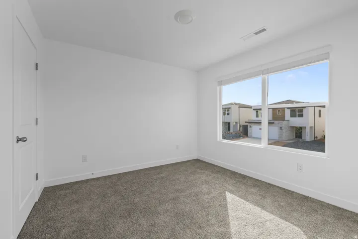 Bright interior space featuring a large window, soft carpeting, and white walls