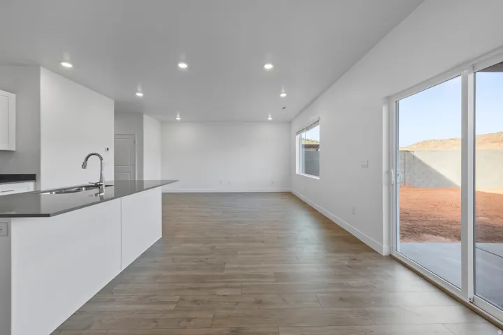 Open-concept living space with wood-finish flooring, recessed lighting, and a kitchen island featuring a sink and gooseneck faucet