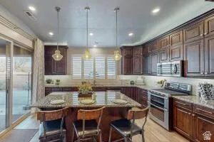 Kitchen featuring an island with stone countertop, dark wood cabinetry, stainless steel appliances, pendant lighting, and wood-finish flooring