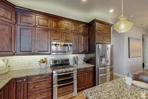Kitchen featuring rich wood cabinetry, stainless steel appliances, granite-style countertops, and a subway tile backsplash