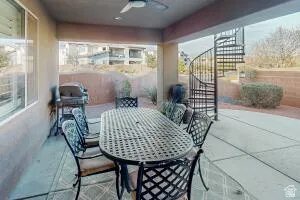 Covered patio with concrete flooring, featuring a black metal spiral staircase, a ceiling fan, and a low retaining wall