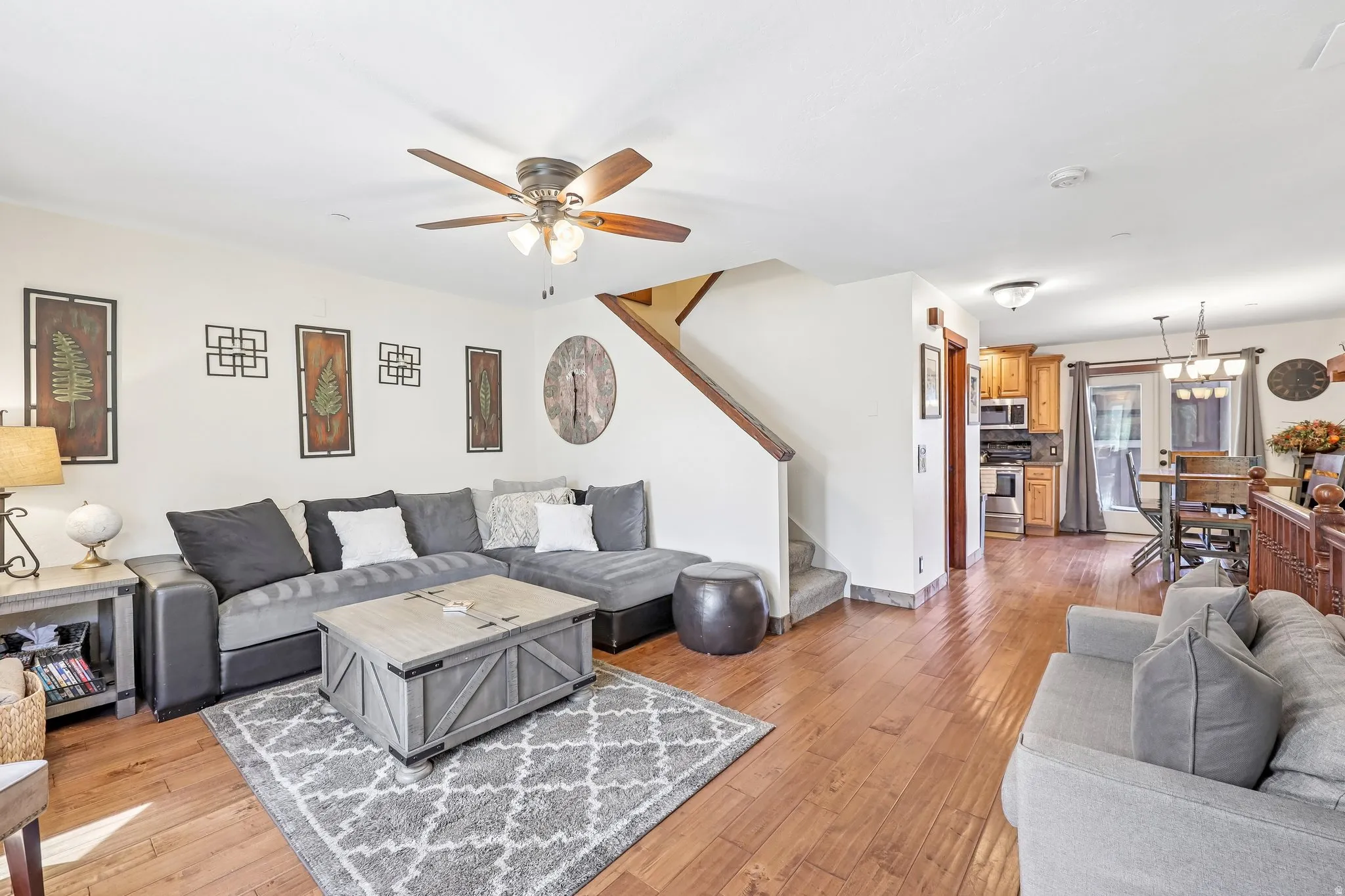 Open-concept living area featuring wood-finish flooring, a ceiling fan, and a staircase with wood railing