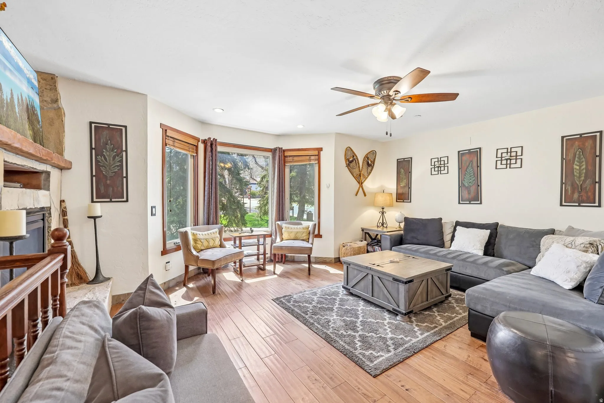 Spacious living area featuring wood-finish flooring, a ceiling fan, and a stone-clad fireplace with a wood mantel
