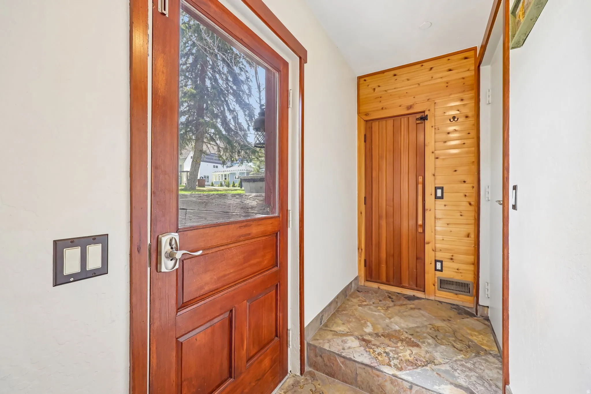 Entryway featuring a wood-panel accent wall, natural stone flooring, and a solid wood door with an inset glass panel