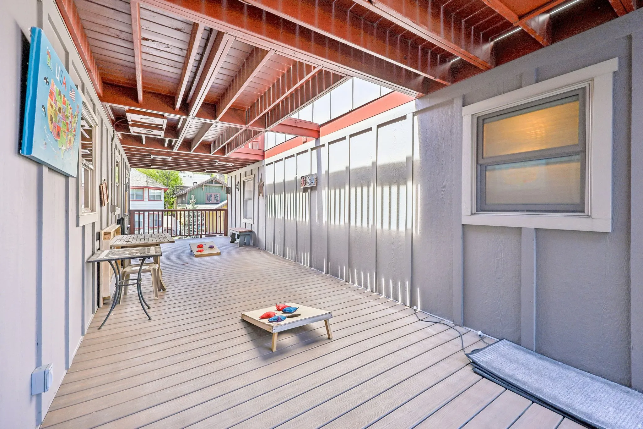 Covered outdoor deck with light gray plank flooring, a slatted ceiling, and an exposed wood beam structure