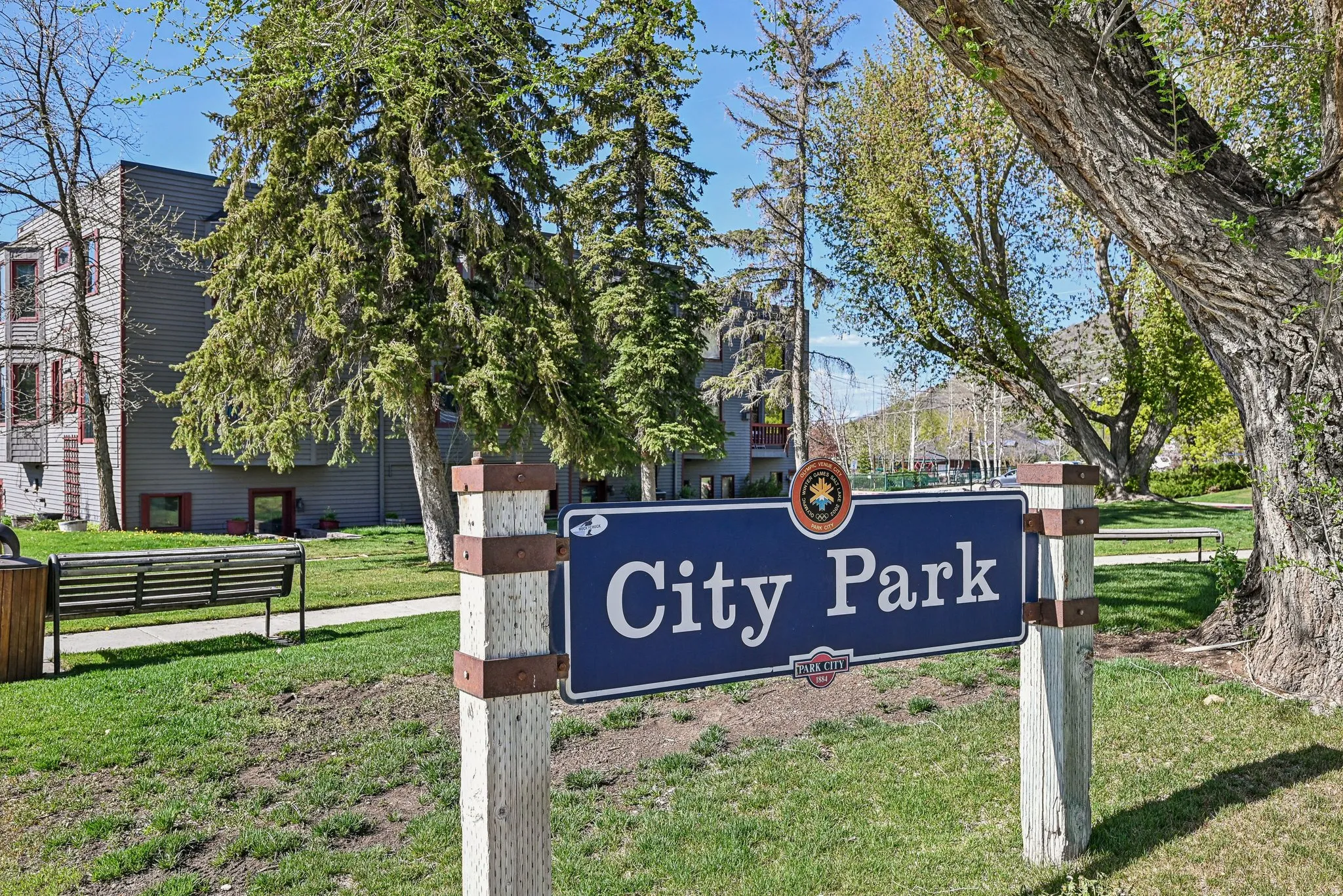 "City Park" signage on a wooden post, set within a green space featuring mature trees and a paved pathway