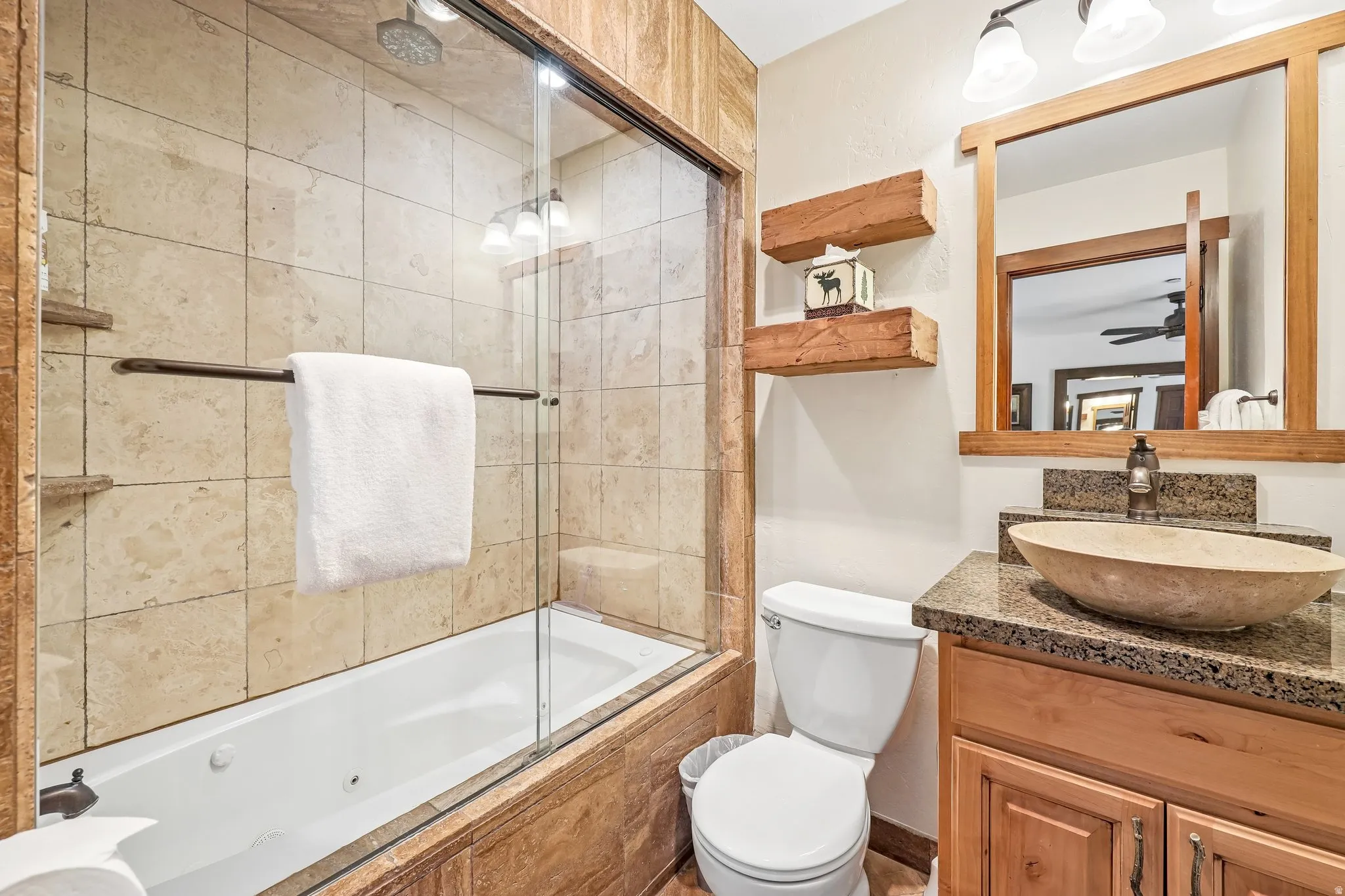 Bathroom featuring a jetted tub with glass enclosure, stone-tiled shower surround, a vessel sink on a granite-look countertop, and a wood-framed mirror