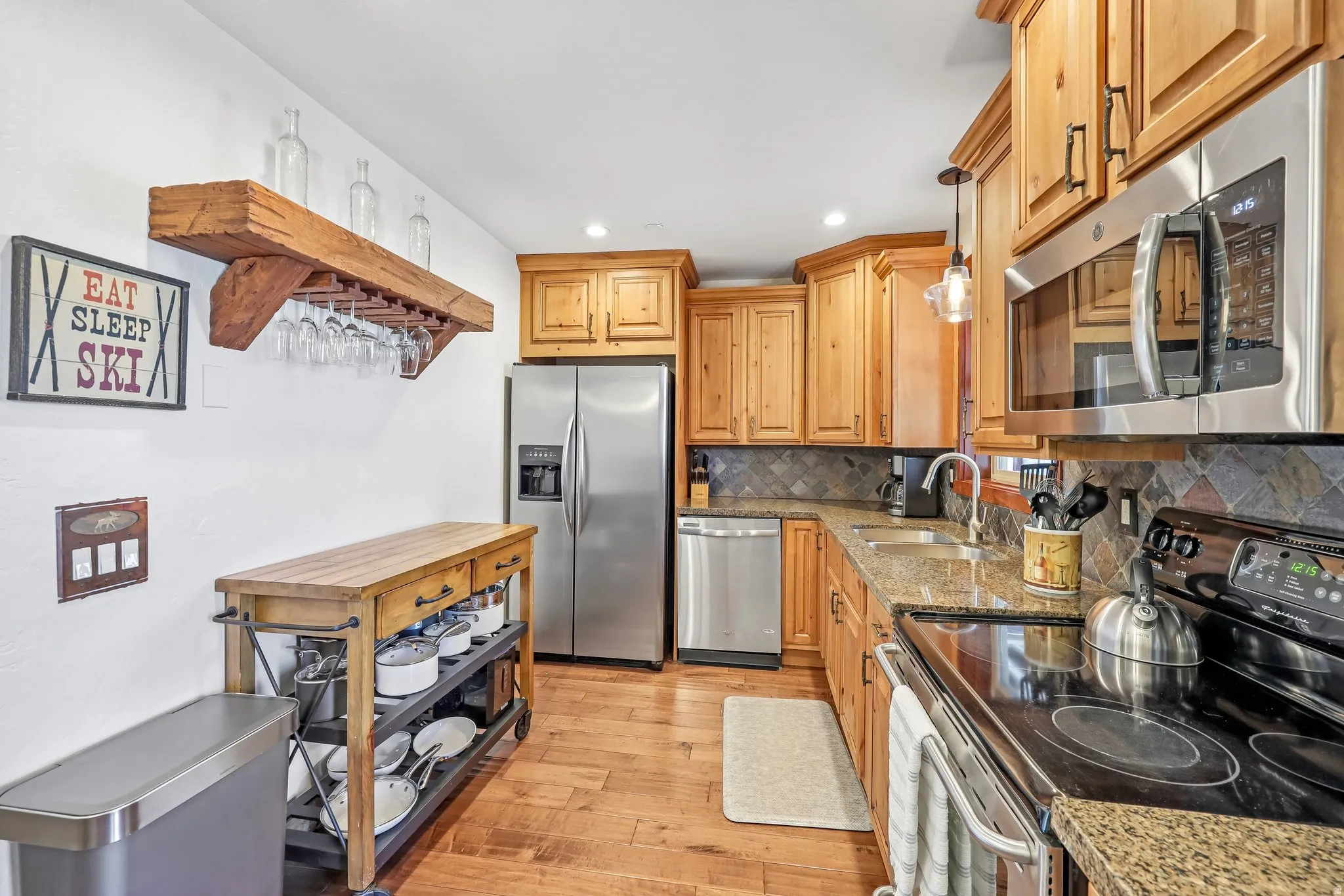 Kitchen featuring wood-finish cabinetry, stainless steel appliances, granite countertops, tile backsplash, and wood-finish flooring