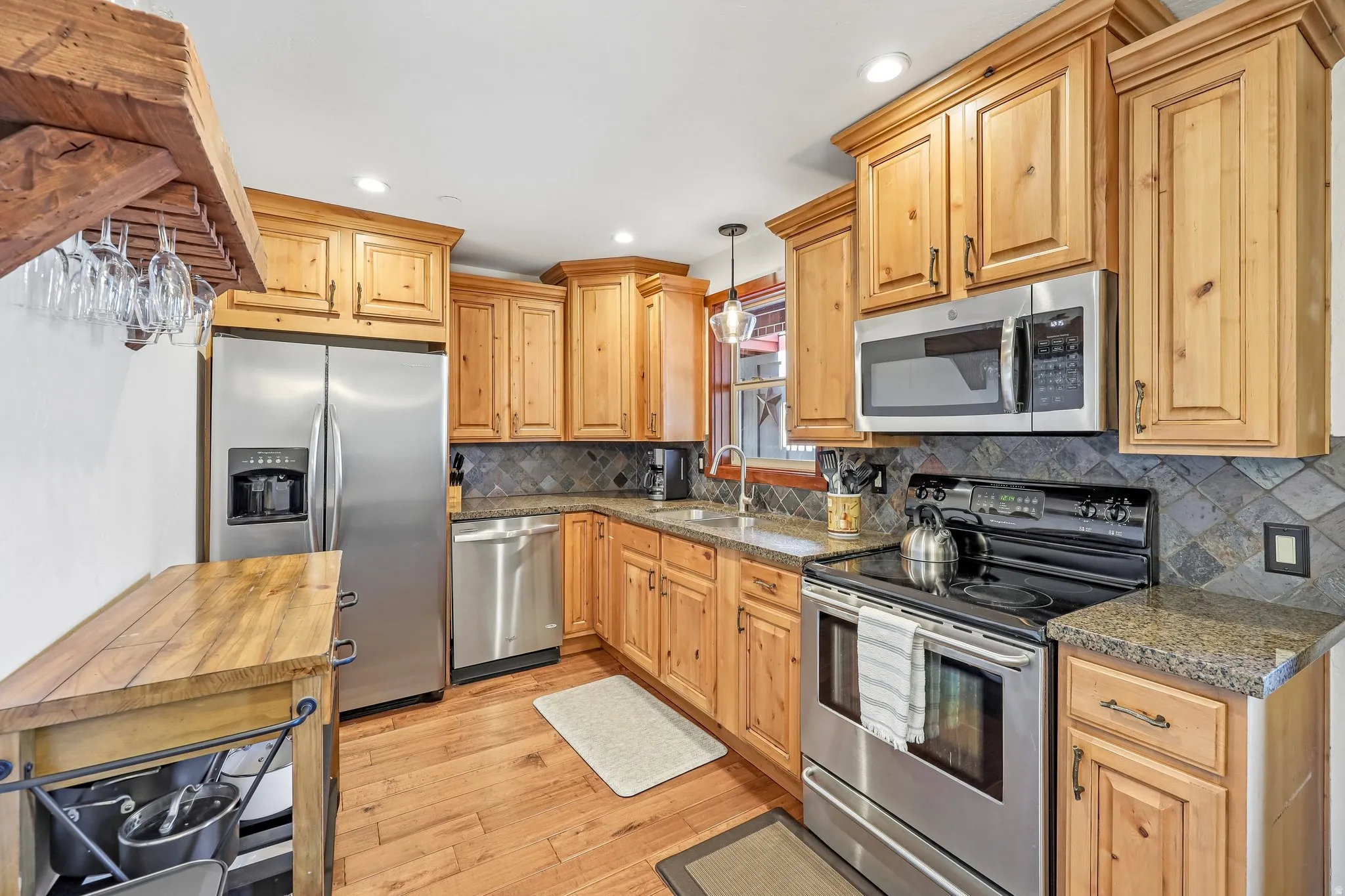 Kitchen featuring natural wood cabinetry, stainless steel appliances, granite-style countertops, a tile backsplash, and wood-finish flooring