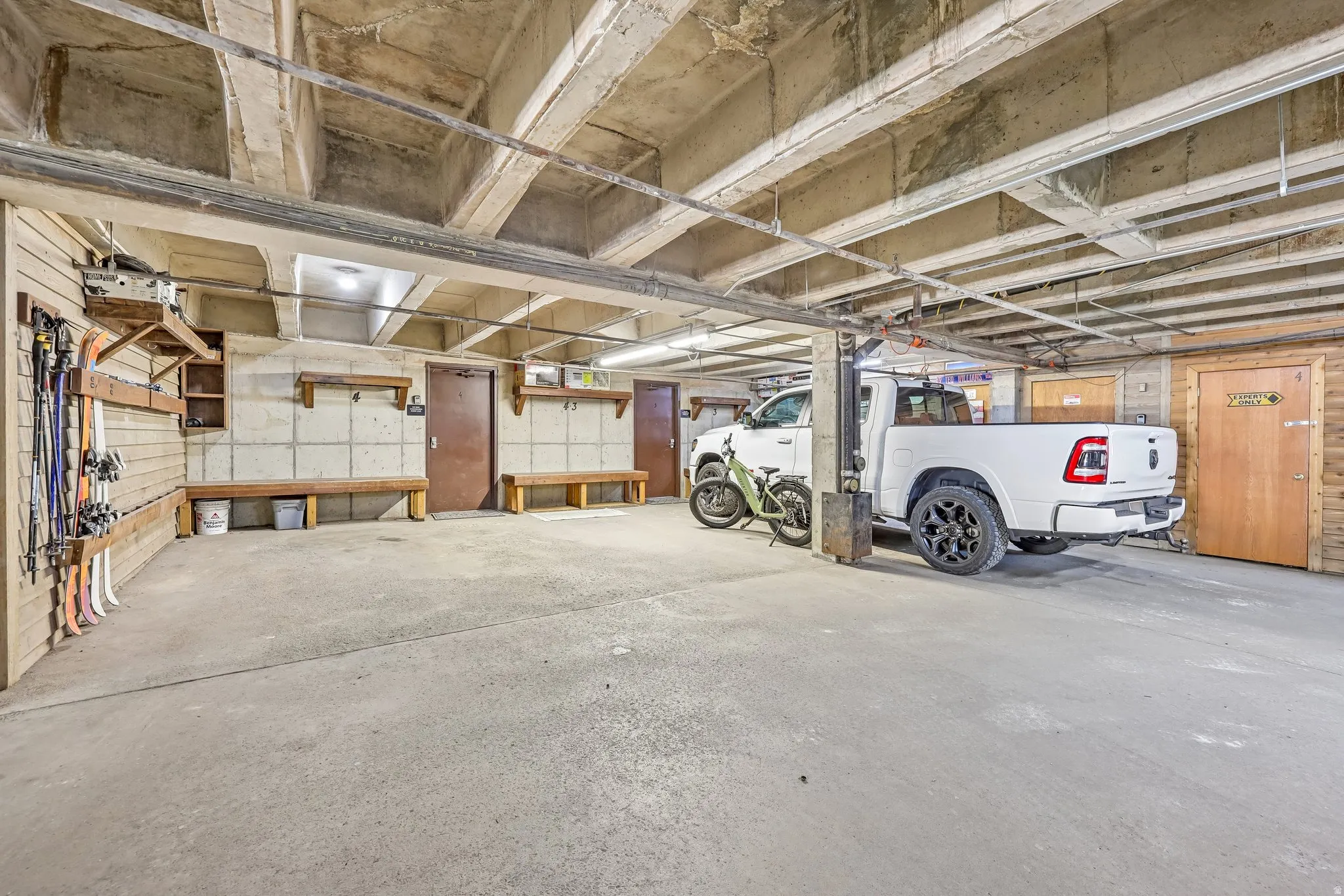 Concrete floor garage space featuring exposed concrete ceiling beams, built-in wooden shelving, and multiple wooden benches