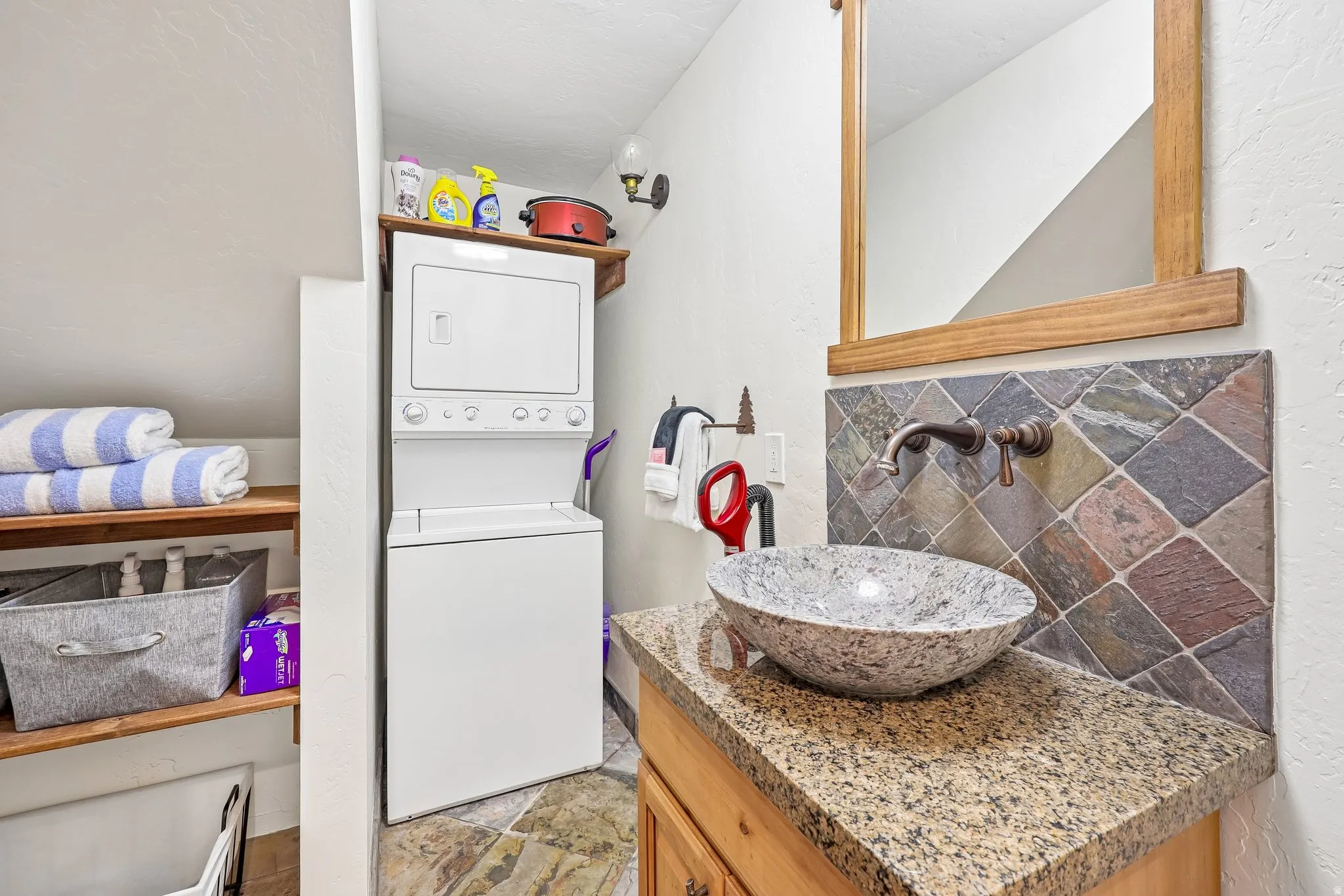 Modern vanity featuring a vessel sink, speckled countertop, and wall-mounted faucet