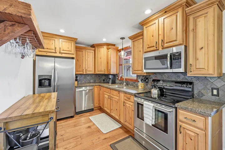 Kitchen featuring natural wood cabinetry, stainless steel appliances, granite-style countertops, a tile backsplash, and wood-finish flooring