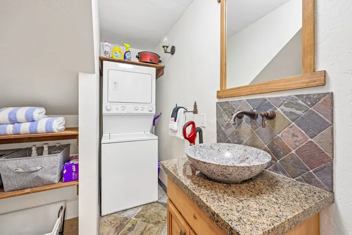 Modern vanity featuring a vessel sink, speckled countertop, and wall-mounted faucet