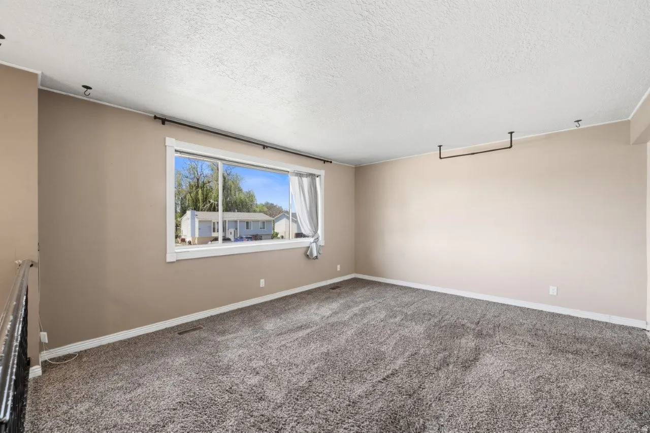 Spacious upper-level living area with carpet, neutral paint, and a bright picture window letting in plenty of natural light. Ready for your personal touch and furniture placement.