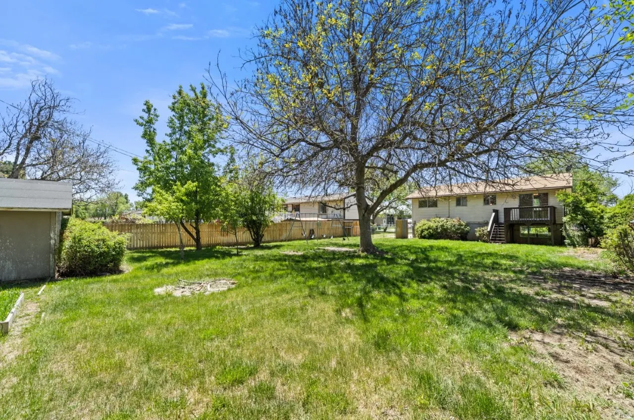 Another look at this generous backyard showing lush green grass, mature trees, a storage shed, and the back deck. Fully fenced and full of possibilities for the right buyer.