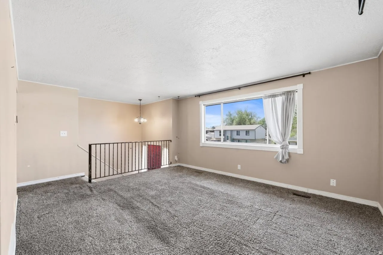 Bright and open living space with carpet, a statement chandelier, and a large picture window that fills the room with natural light. The open staircase and neutral palette give buyers a true blank canvas to work with.