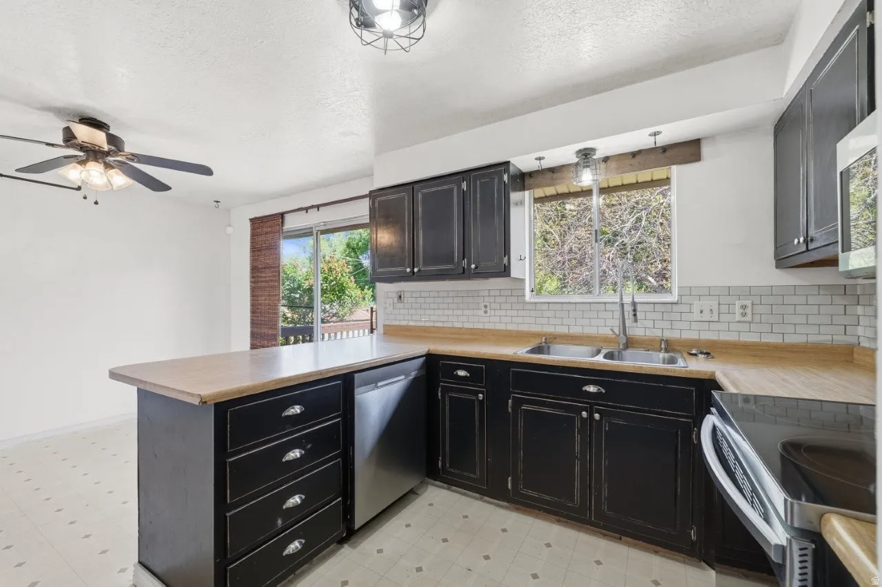 Bright kitchen with double sink, stainless dishwasher, countertops, and subway tile backsplash. Two windows plus a sliding glass door flood the space with natural light and provide easy access to the back deck.