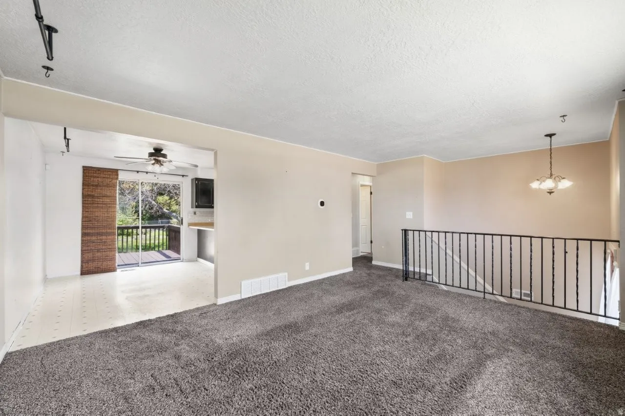 Spacious upper-level living area flows openly into the kitchen and dining space, with a ceiling fan, pendant light, and sliding glass door leading to the back deck. The wrought iron staircase railing adds a classic touch and the open layout makes this hom